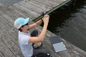 Woman sitting on dock pointing smartphone up to the sky