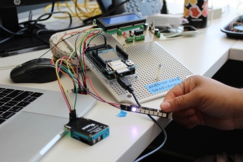 A hand holds an LED light strip hooked up to circuits and a test board on a desk.