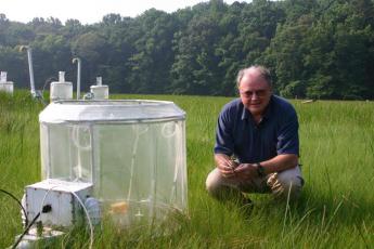 Smithsonian plant scientist Bert Drake kneels beside a CO2 chamber in the Global Change Research Wetland