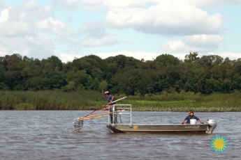 2 men on a small boat in the Patuxent River: 1 man at the edge with a fishing net & the other man at the other end, driving