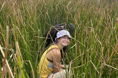 Taylor kneeling in tall marsh grass