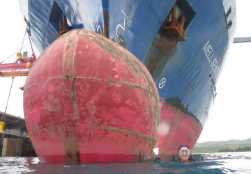 A diver gets ready to dive under the bulbous bow of a ship. 