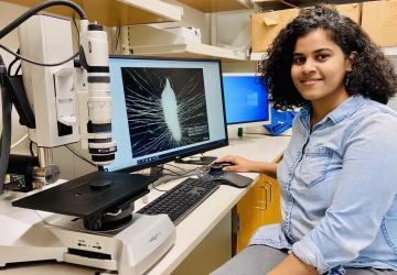 Eranga Wettewa, a young woman of Southeast Asian descent, sits by a computer screen with a microscopic image of orchids and fung