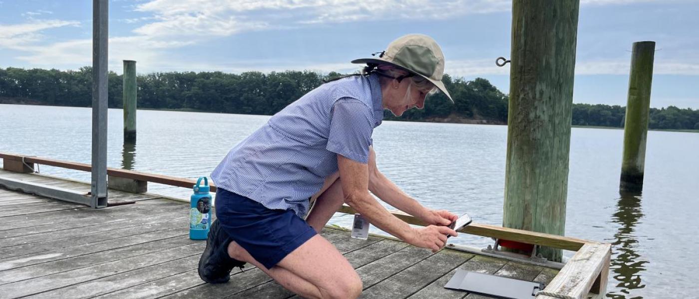 Women bending down on a dock taking a picture of a gray card with her phone