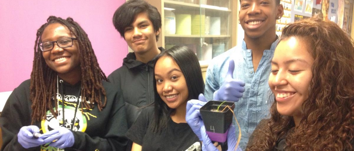 five high school students smiling at the camera holding up materials from the project