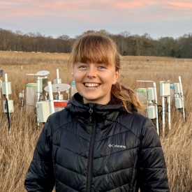 Abigail Lewis standing in a marsh with experimental chambers